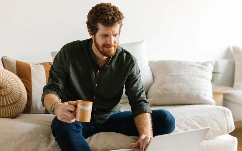 a man sitting on a couch with a laptop and a cup of coffee